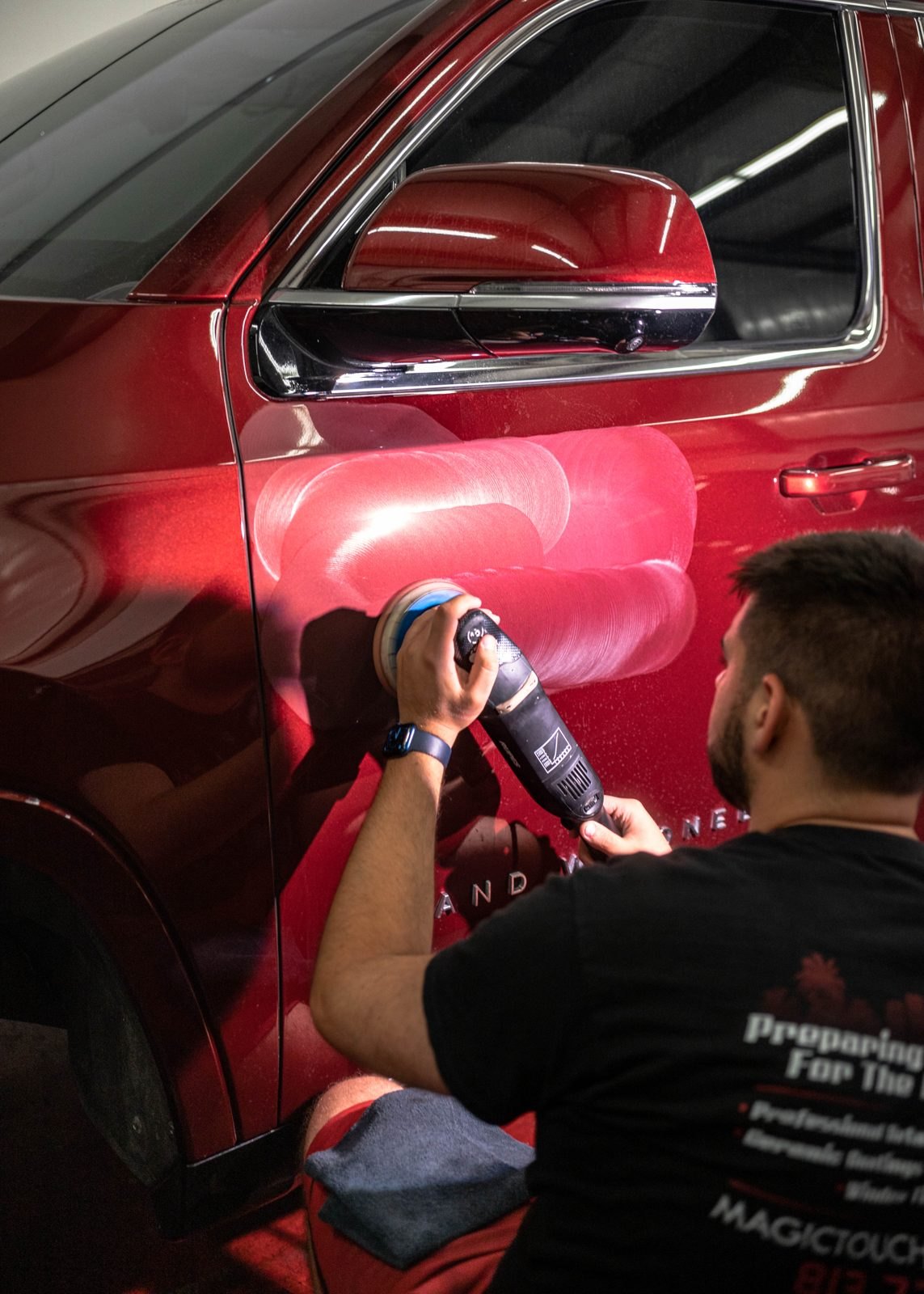 Detailer machine-polishing the door of a red Jeep